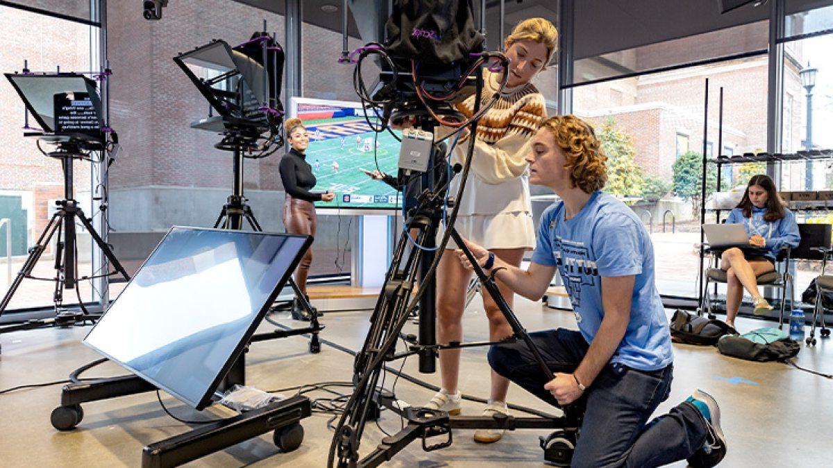 Two students working together by a video camera inside of a TV studio.